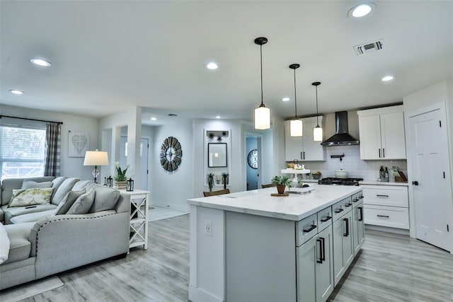 kitchen featuring light wood-style flooring, open floor plan, backsplash, a center island, and wall chimney exhaust hood