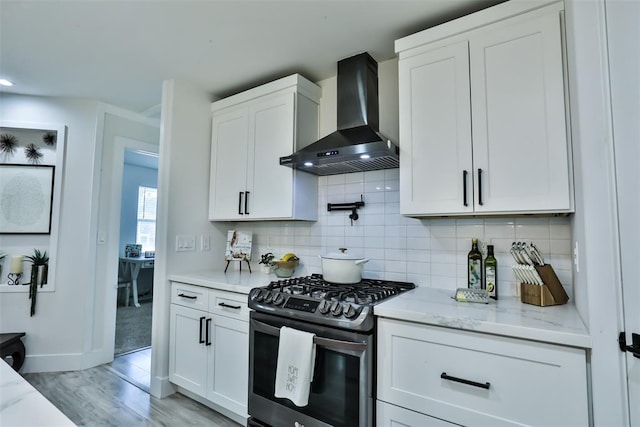 kitchen with wall chimney exhaust hood, stainless steel gas range oven, backsplash, and white cabinetry