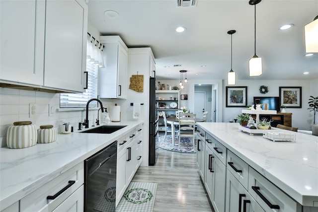 kitchen featuring light stone counters, a sink, white cabinetry, black dishwasher, and pendant lighting