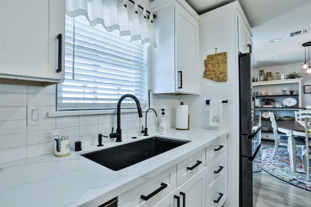 kitchen with light stone counters, freestanding refrigerator, a sink, white cabinetry, and backsplash