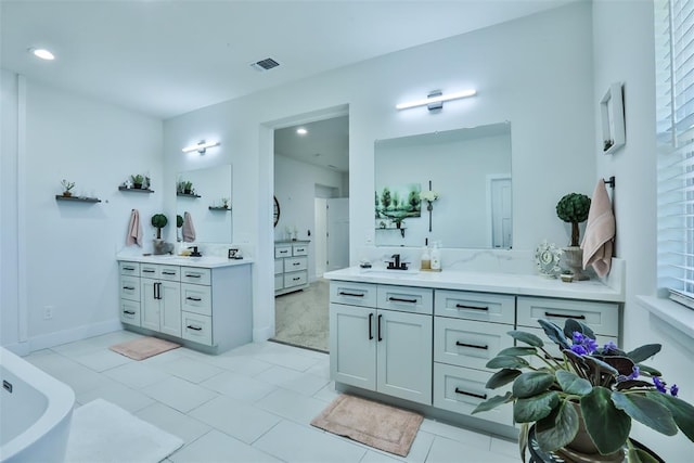 bathroom with a sink, a freestanding tub, two vanities, and visible vents