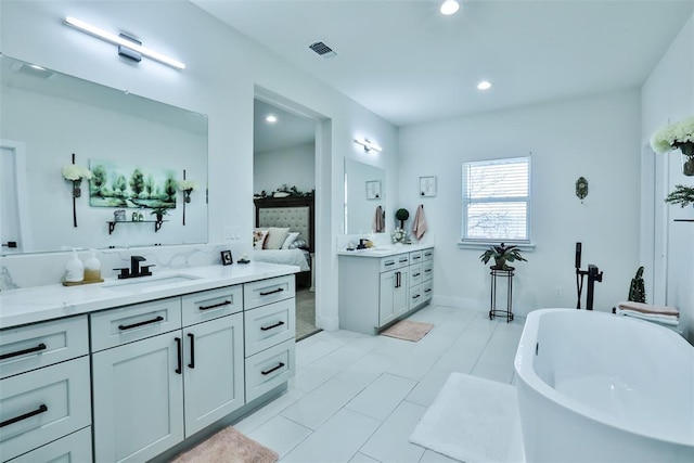 ensuite bathroom with two vanities, visible vents, a freestanding bath, connected bathroom, and a sink