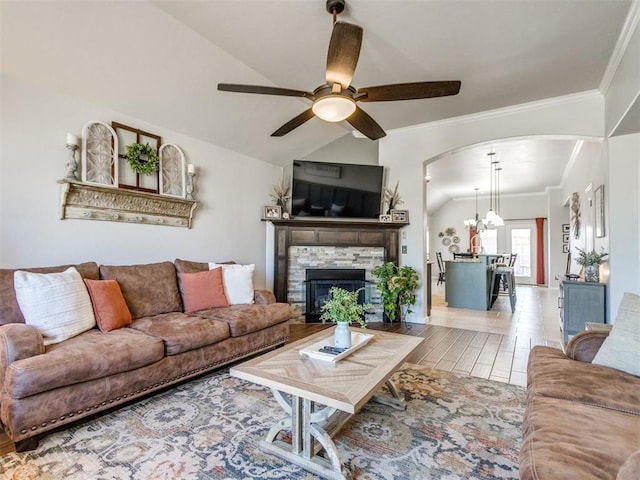 living area with a ceiling fan, a stone fireplace, crown molding, arched walkways, and vaulted ceiling