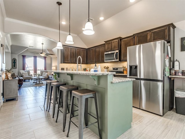 kitchen with ceiling fan, light stone counters, dark brown cabinetry, arched walkways, and stainless steel appliances