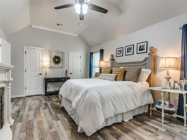 bedroom with ceiling fan, visible vents, a fireplace, vaulted ceiling, and wood finished floors