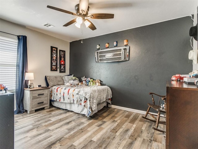 bedroom with ceiling fan, a wall mounted AC, wood finished floors, and visible vents