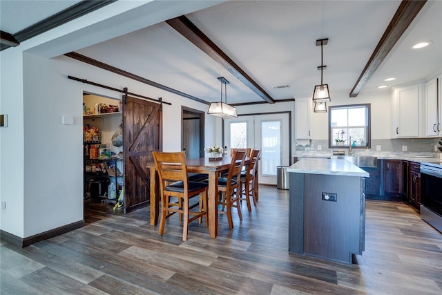 kitchen with a barn door, decorative backsplash, white cabinets, a kitchen island, and beam ceiling