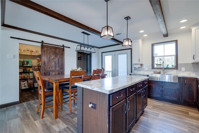 kitchen featuring wood finished floors, beamed ceiling, light countertops, white cabinetry, and a sink