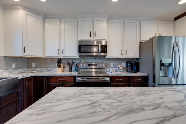 kitchen with appliances with stainless steel finishes, white cabinetry, decorative backsplash, and light stone countertops