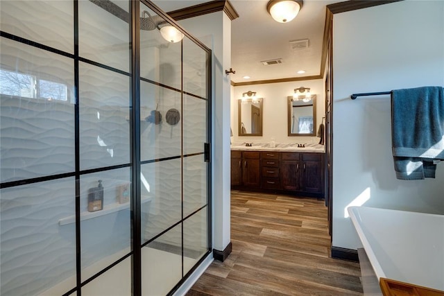 full bathroom featuring a stall shower, ornamental molding, wood finished floors, a freestanding bath, and a sink