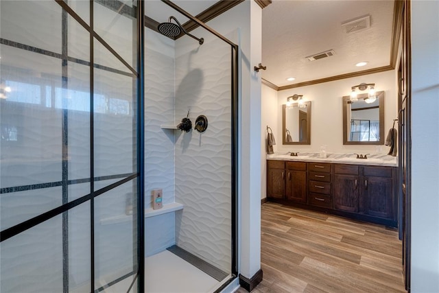 bathroom featuring a sink, wood finished floors, visible vents, ornamental molding, and a shower stall