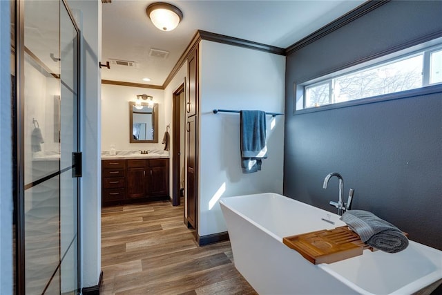 full bathroom with a freestanding bath, ornamental molding, wood finished floors, and vanity