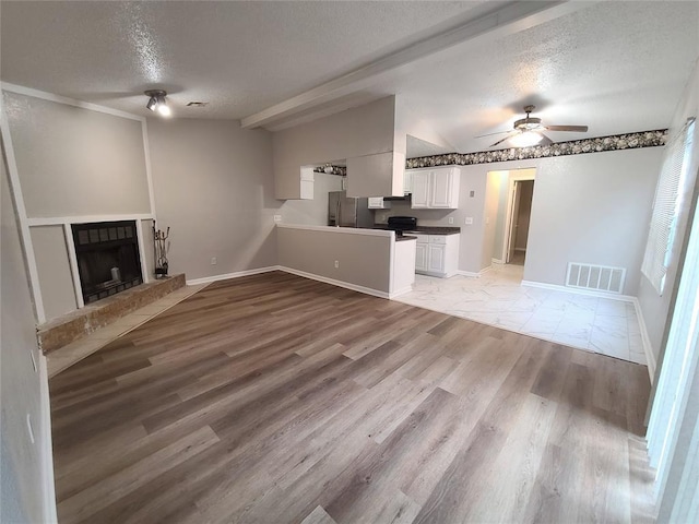 unfurnished living room with visible vents, a fireplace with raised hearth, a textured ceiling, and ceiling fan