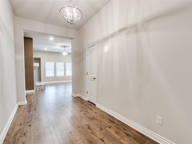 interior space featuring wood-type flooring, baseboards, and ceiling fan with notable chandelier