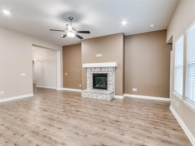 unfurnished living room featuring a brick fireplace, wood finished floors, a ceiling fan, and baseboards