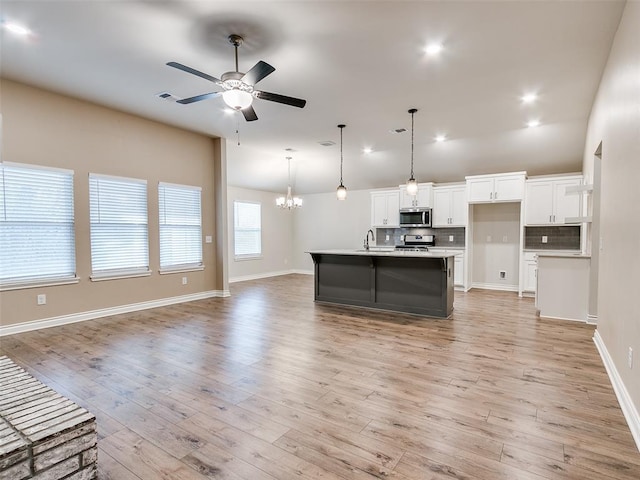 kitchen featuring backsplash, appliances with stainless steel finishes, open floor plan, white cabinetry, and ceiling fan with notable chandelier