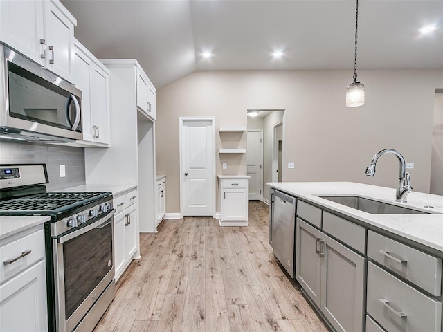 kitchen featuring stainless steel appliances, a sink, light wood-type flooring, backsplash, and decorative light fixtures