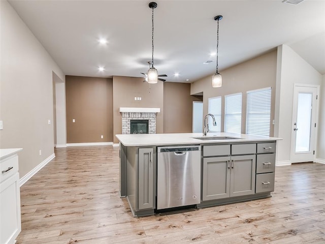 kitchen featuring gray cabinetry, a fireplace, a sink, light countertops, and stainless steel dishwasher