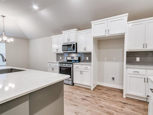 kitchen featuring light wood finished floors, appliances with stainless steel finishes, decorative light fixtures, vaulted ceiling, and a sink