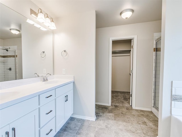 bathroom with a walk in closet, double vanity, a sink, a shower stall, and baseboards