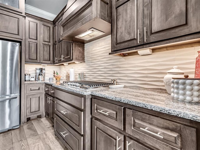 kitchen featuring dark brown cabinetry, tasteful backsplash, custom range hood, and appliances with stainless steel finishes