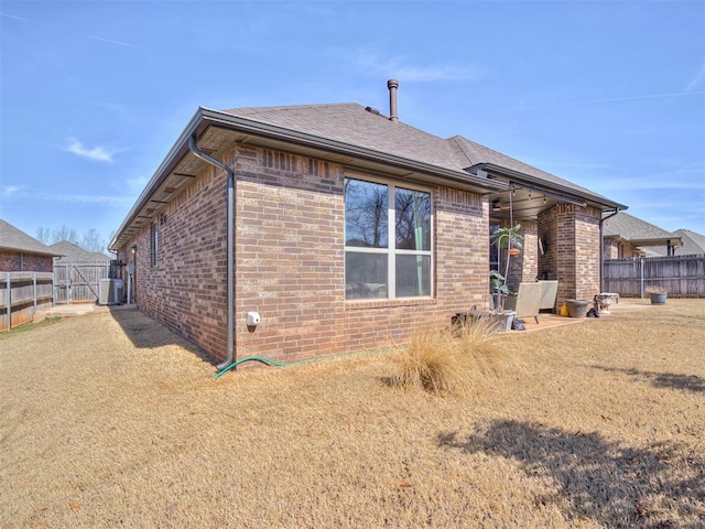 rear view of house with cooling unit, a gate, brick siding, and fence