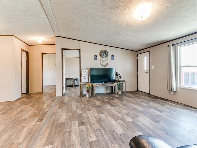 unfurnished living room featuring light wood-style floors, ornamental molding, and a textured ceiling