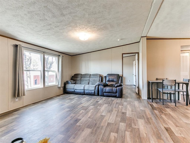 living room featuring crown molding, a textured ceiling, a decorative wall, and wood finished floors