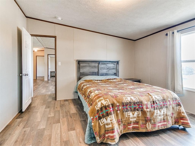 bedroom featuring a textured ceiling, ornamental molding, and light wood-style floors