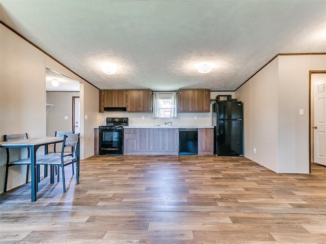 kitchen with brown cabinetry, light countertops, a textured ceiling, light wood-type flooring, and black appliances