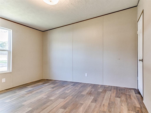 spare room featuring light wood-style flooring, crown molding, and a textured ceiling