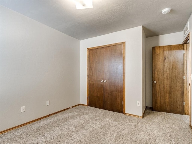 unfurnished bedroom with a textured ceiling, carpet floors, visible vents, baseboards, and a closet