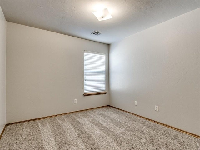 spare room featuring light colored carpet, visible vents, a textured ceiling, and baseboards