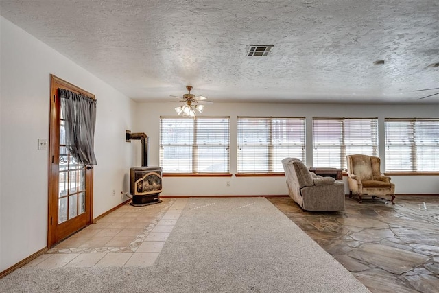 unfurnished room featuring a ceiling fan, a wealth of natural light, a wood stove, and visible vents