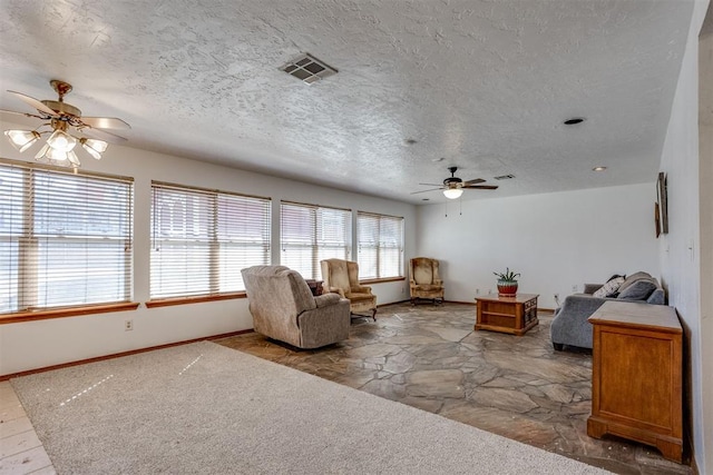 living area with visible vents, ceiling fan, a textured ceiling, and baseboards