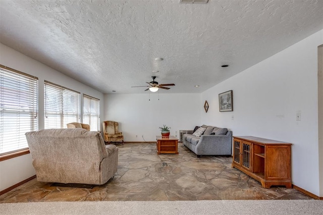 living area with a textured ceiling, a ceiling fan, and baseboards