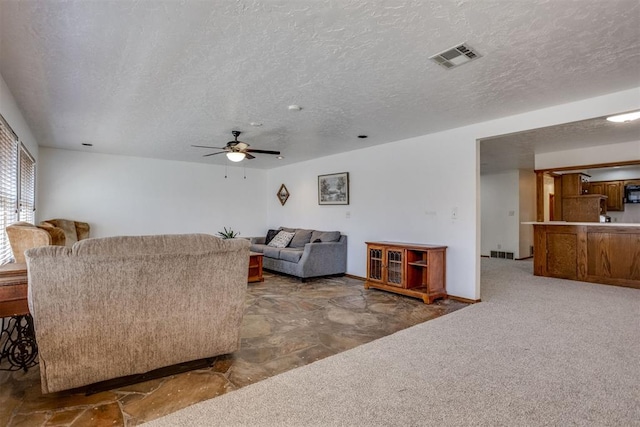 carpeted living room featuring a ceiling fan, visible vents, and a textured ceiling