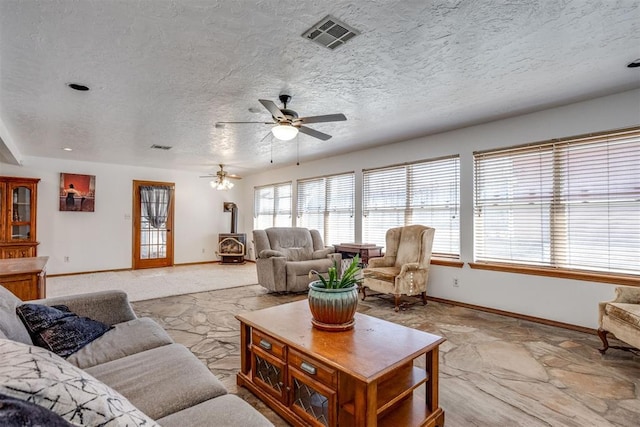 living area with a wood stove, baseboards, visible vents, and a textured ceiling