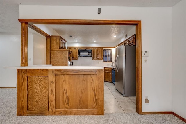 kitchen featuring baseboards, brown cabinetry, freestanding refrigerator, a peninsula, and black microwave