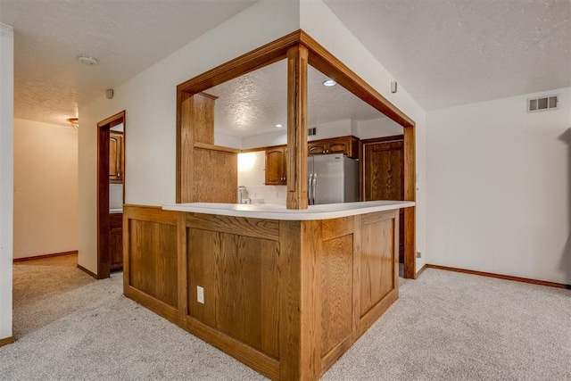 kitchen with freestanding refrigerator, visible vents, light carpet, and a textured ceiling