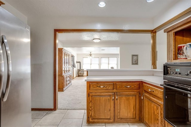 kitchen featuring light countertops, brown cabinetry, freestanding refrigerator, light tile patterned flooring, and black oven