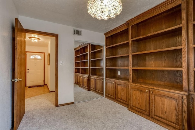 corridor with a textured ceiling, baseboards, visible vents, and light colored carpet