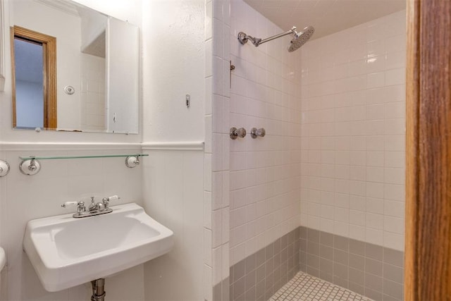 bathroom featuring a sink, wainscoting, a tile shower, and toilet