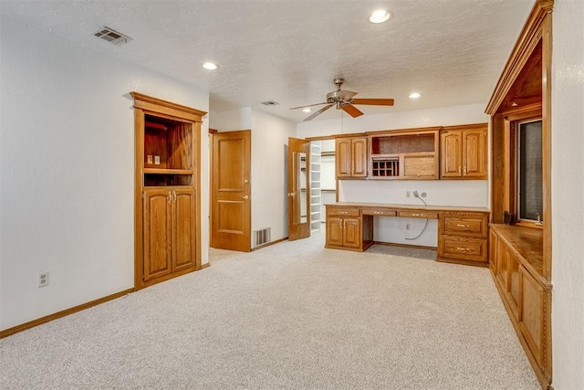 kitchen featuring a textured ceiling, visible vents, brown cabinets, open shelves, and built in desk