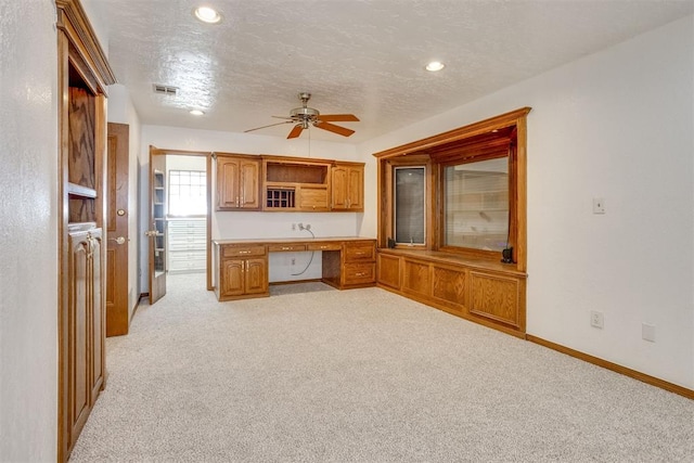 kitchen featuring light colored carpet, brown cabinets, a textured ceiling, open shelves, and built in desk