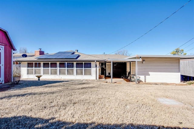 back of house featuring a yard, a sunroom, and roof mounted solar panels