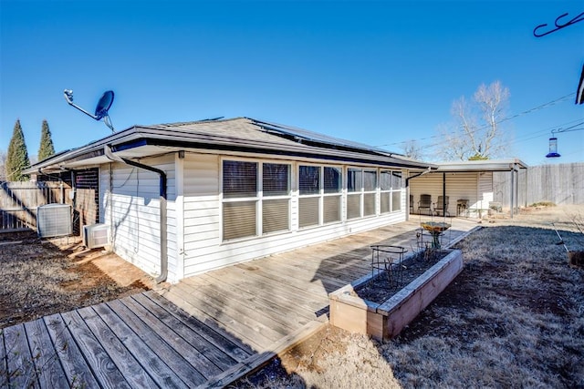 rear view of property featuring a vegetable garden, fence, a deck, roof mounted solar panels, and central AC