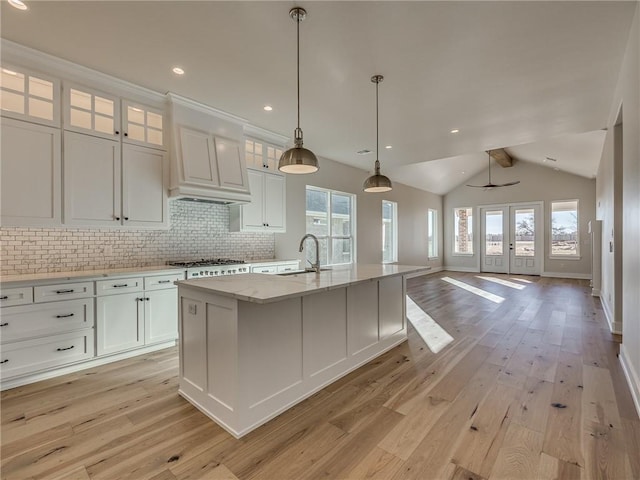 kitchen with an island with sink, light wood-style floors, white cabinetry, and decorative backsplash