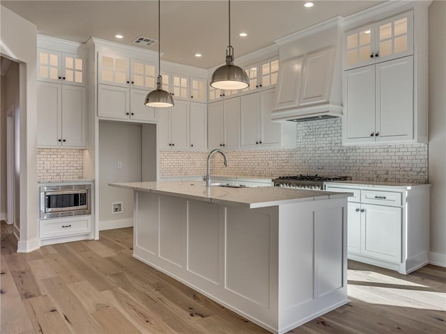 kitchen featuring visible vents, stainless steel microwave, white cabinets, a sink, and premium range hood