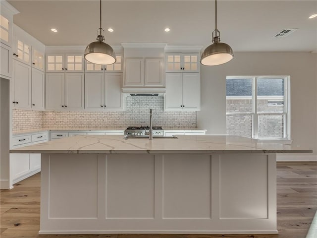 kitchen featuring a center island with sink, visible vents, white cabinets, light stone counters, and light wood-type flooring